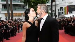 Aktor senior Mel Gibson dan pacarnya barunya saat berpose di karpet merah acara penutupan Festival Film Cannes ke-69 di Prancis, 22 Mei 2016. Pasangan romantis ini tak segan berbagi ciuman di depan umum. (Anne-CHRISTINE POUJOULAT/AFP)