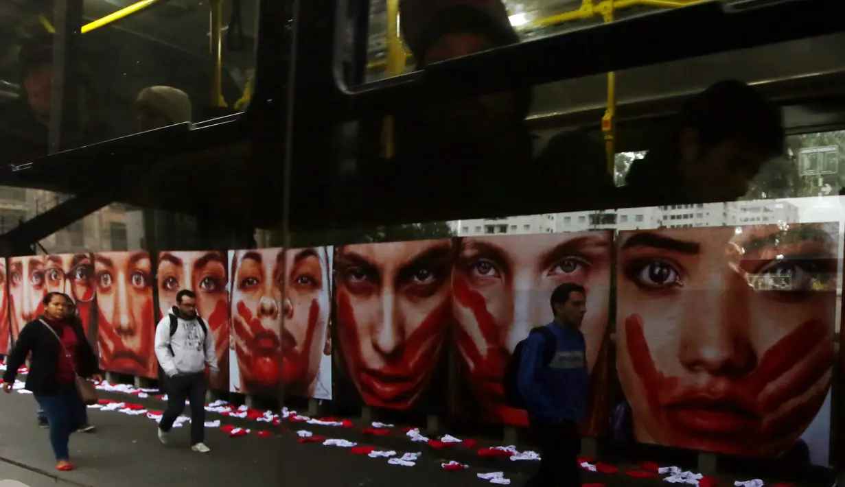 Warga berjalan disamping deretan foto wanita dengan wajah bercat merah di Sao Paulo Art Museum, Brasil , 10 Juni 2016. Ini juga sebagai protes organisasi non -pemerintah yang dinamakan Rio de Paz. (REUTERS / Paulo Whitaker)