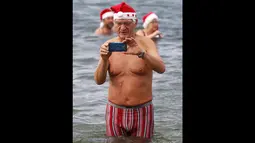 Puluhan anggota klub renang es "Berliner Seehunde" merayakan Natal dengan berenang di danau Orankesee, Berlin (25/12/2014). Tampak, seorang anggota klub "Berliner Seehunde" mengambil gambar dengan telepon genggamnya. (REUTERS/Fabrizio Bensch)