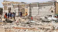 Orang-orang berjalan di sebelah rumah yang hancur dan puing-puing mobil menyusul serangan oleh militan Al-Shabaab selama penyerangan ke kantor polisi di pinggiran Mogadishu, Somalia (16/2/2022). (AFP/Hassan Ali Elmi)