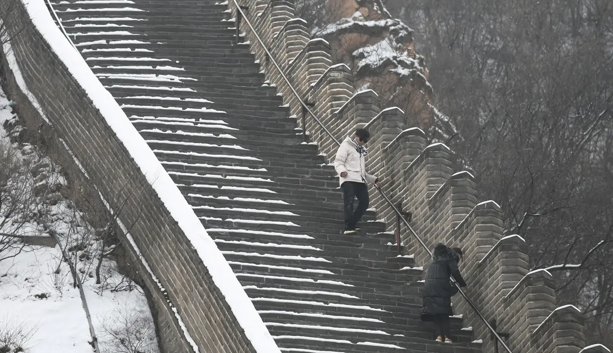 Dua wisatawan menuruni anak tangga saat menikmati liburan musim dingin di Tembok Besar China yang diselimuti salju di utara Beijing (6/1/2020). (AFP/Greg Baker)