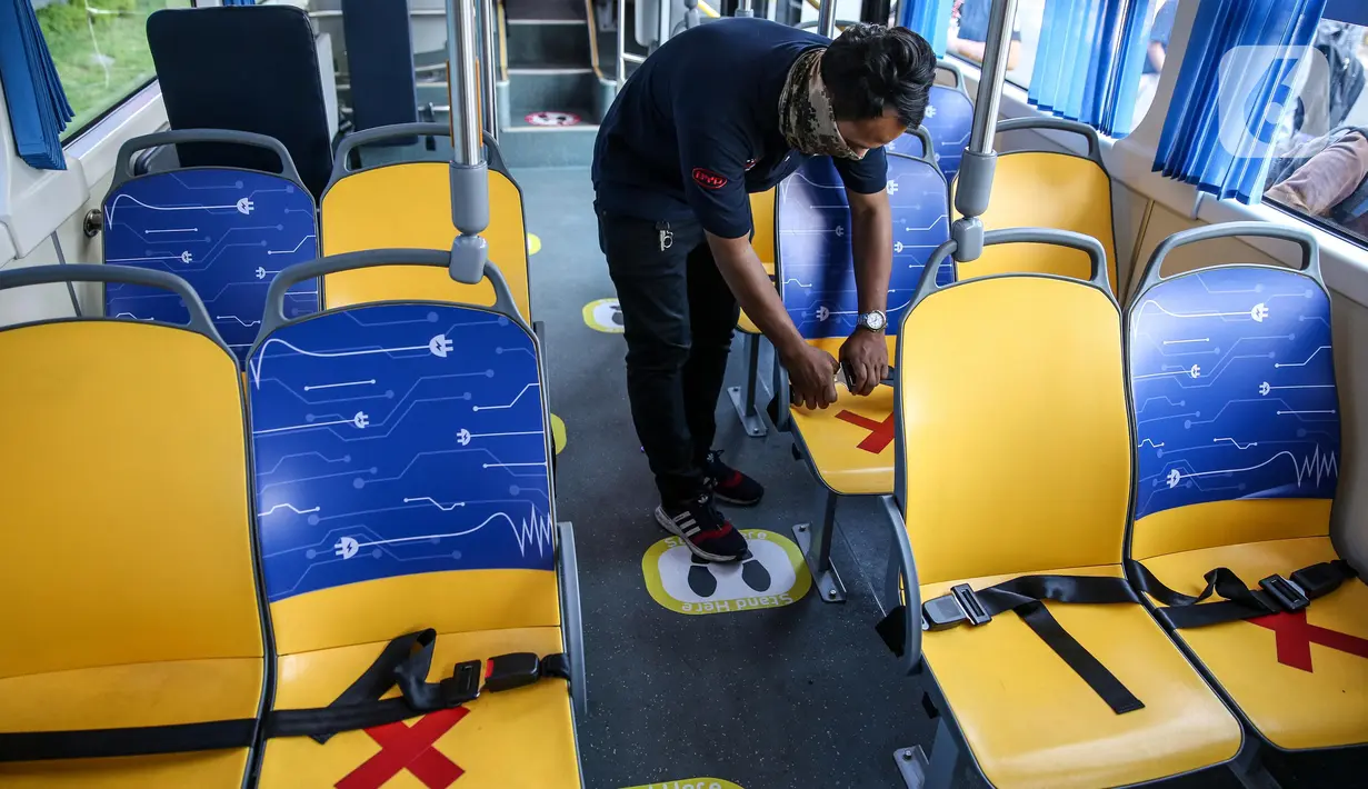 Petugas memasang stiker panduan jarak pada bangku bus listrik Transjakarta di Kantor Pusat Transjakarta, Senin (6/7/2020). Layanan ini akan beroperasi setiap hari, mulai pukul 10.00-20.00 WIB dan berhenti di halte-halte Non-BRT di sepanjang rute Blok M hingga Balai Kota. (Liputan6.com/Faizal Fanani)