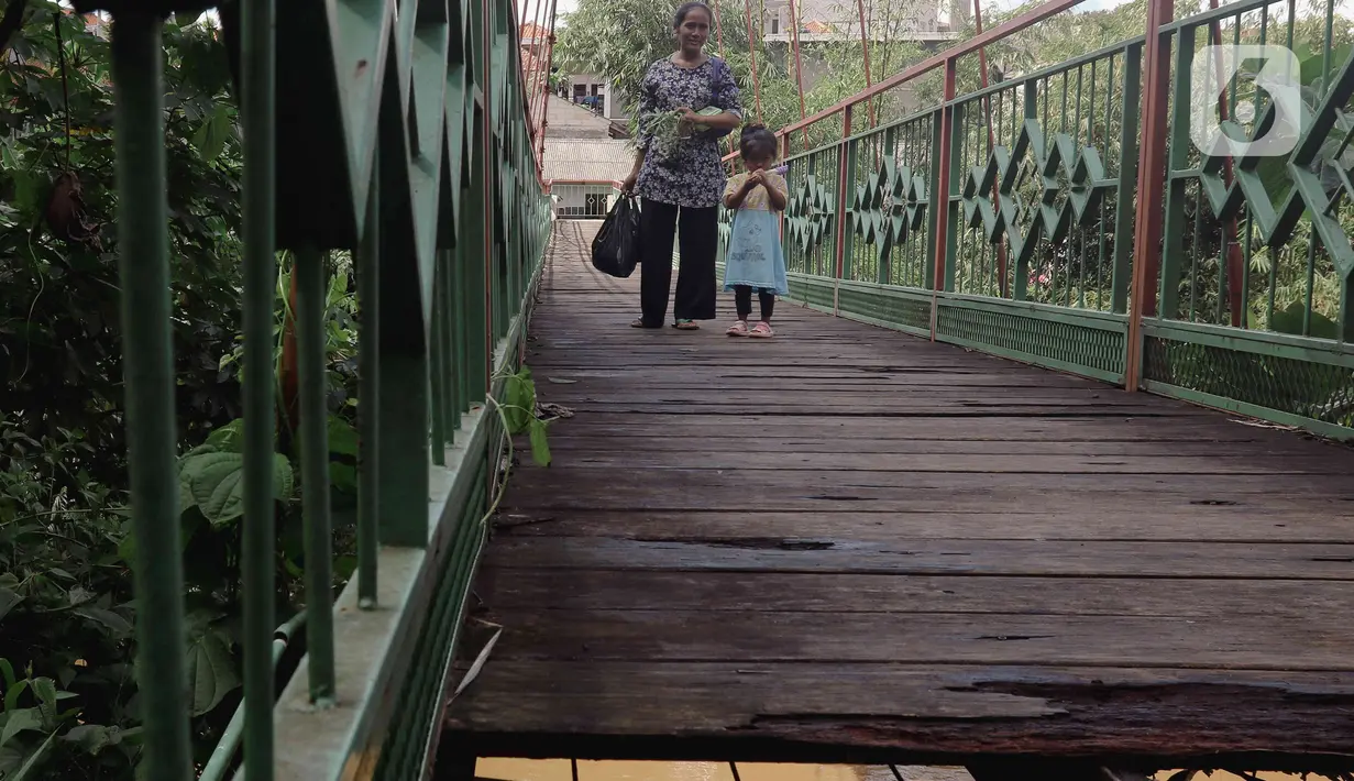 Seorang ibu bersama anak kecil melintasi jembatan yang berlubang di Jembatan Wiratman, Srengseng Sawah, Jakarta, Sabtu (12/3/2022). Jembatan tersebut menghubungkan Kelurahan Srengseng Sawah, Jakarta Selatan dengan Kelurahan Pasir Gunung Selatan, Depok. (Liputan6.com/Herman Zakharia)