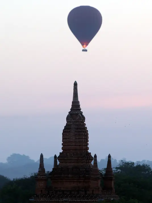 Sebuah balon udara terbang di atas kuil tua selama matahari terbit di Bagan, distrik Nyaung U, Myanmar tengah (16/12). Balon udara diterbangkan di pagi hari berdasarkan arah angin dari Oktober hingga April. (AP Photo/Aung Shine Oo)
