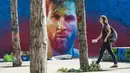 Seorang wanita melintasi mural bergambar wajah bintang Barcelona, Lionel Messi, yang terdapat di Barcelona, Catalonia, Sabtu (17/6/2017). (AFP/Josep Lago)