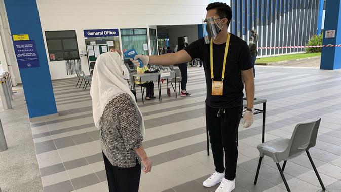 Petugas memeriksa suhu tubuh pemilih yang memberikan suara dalam pemilu di TPS Dunearn Secondary School, Singapura Jumat (10/7/2020). Pemilu di tengah pandemi COVID-19, warga Singapura memberikan suara mereka dengan mengenakan masker dan sarung tangan plastik. (AP Photo/Royston Chan)
