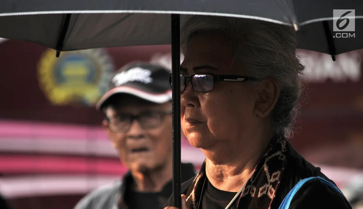 Seorang ibu yang tergabung dalam Jaringan Solidaritas Korban untuk Keadilan (JSKK) mengenakan pakaian dan payung hitam saat mengikuti Aksi Kamisan di depan Istana Negara, Jakarta, Kamis (2/8). (Merdeka.com/Iqbal Nugroho)