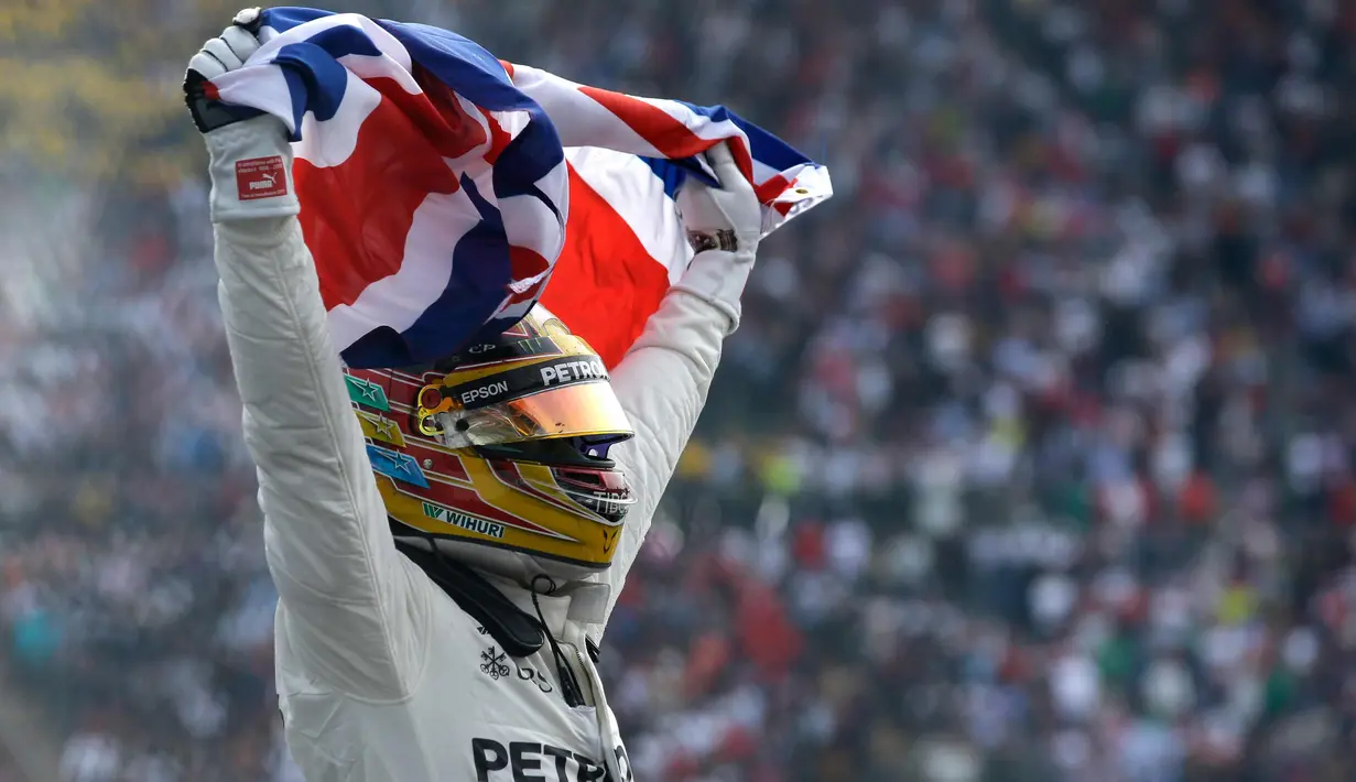 Lewis Hamilton membentangkan bendera negaranya saat merayakan kemenangannya meraih juara dunia F1 untuk yang ke empat kalinya di Autodromo Hermanos Rodrigue, Meksiko (29/10). (AP Photo / Moises Castillo)