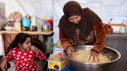 Di setiap negara, roti ini bisa memiliki variasi bentuk dan rasa yang sedikit berbeda. Tampak dalam foto, seorang wanita mengaduk adonan saat menyiapkan biskuit tradisional "kaak" yang berbentuk cincin menjelang Idul Fitri, hari raya yang menandai berakhirnya bulan puasa suci Ramadan, di Kota Gaza pada 16 Maret 2026. (Omar AL-QATTAA/AFP)
