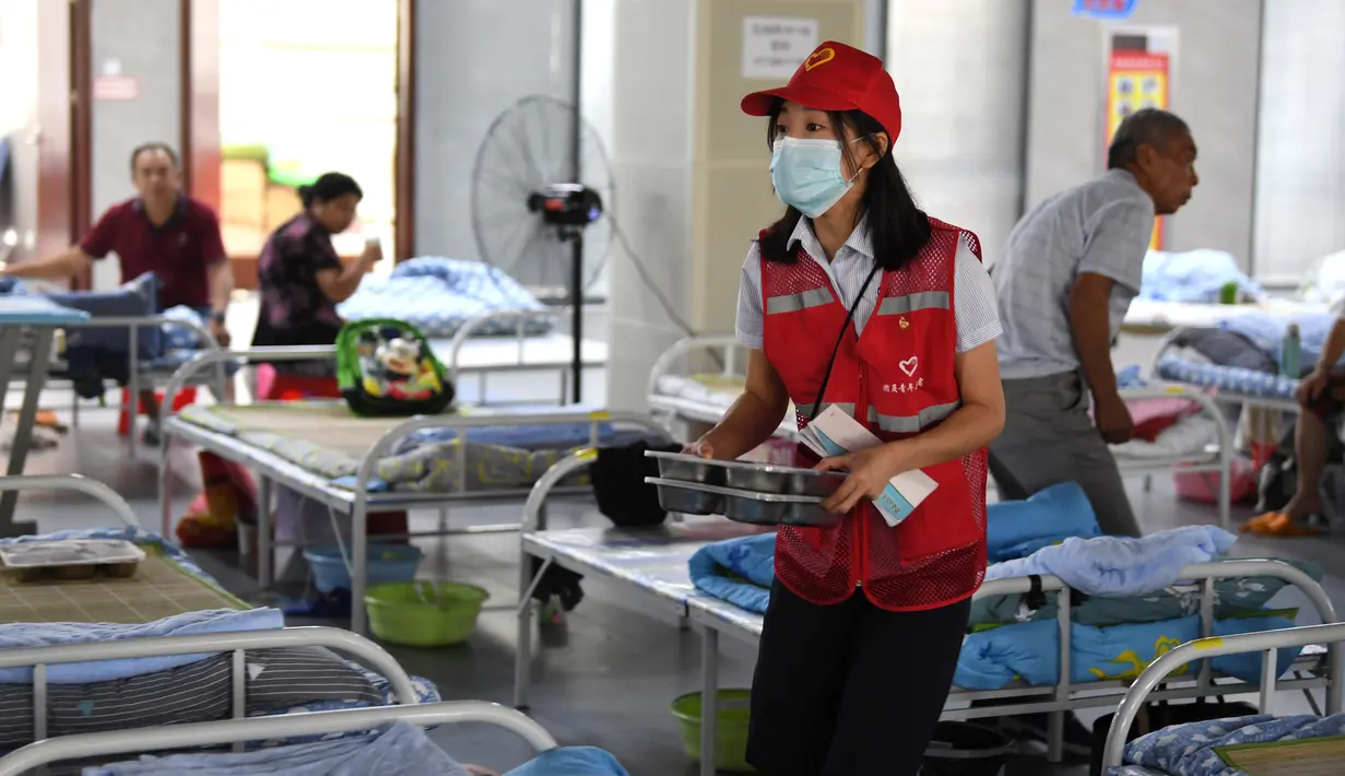 Sukarelawan membagikan makanan untuk penduduk desa di tempat pengungsian sementara Sekolah Menengah No.168, Hefei, Provinsi Anhui, China, Rabu (29/7/2020). Makanan gratis, konseling psikologis, dan bantuan kehidupan sehari-hari disediakan di tempat pengungsian sementara tersebut. (Xinhua/Liu Junxi)