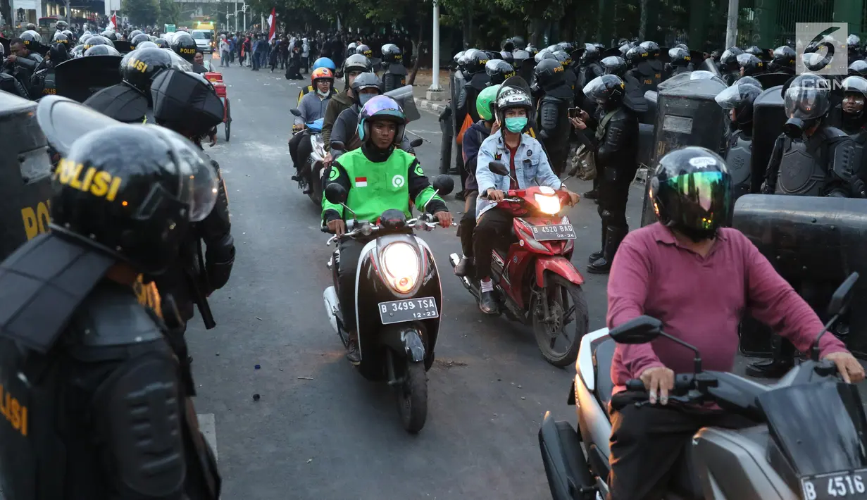 Kendaraan melintas di antara polisi yang berjaga di sekitaran Stasiun Palmerah, Jakarta, Senin (30/9/2019). Jalur di kawasan itu telah dibuka, namun kendaraan harus berhati-hati karena banyaknya batu sisa bentrokan massa di belakang gedung DPR yang berakhir ricuh. (Liputan6.com/Angga Yuniar)