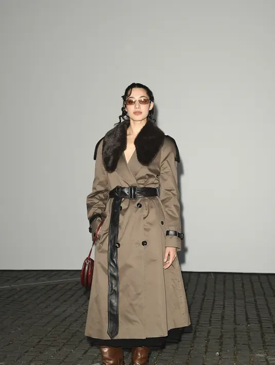 Ameera Khan tampil mengenakan trench coat khaki dengan kerah bulu cokelat tebal. Dipadu sabuk kulit hitam yang dililit vertikal, kacamata rectangle bertona cokelat, tas mini merah dan boots kulit cokelat bertumit tinggi. [dok. Burberry]