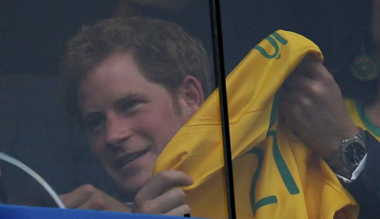 Dari balik kaca pelindung, sambil terus memegangi kaos Timnas Brasil, Pangeran Harry melihat langsung aksi Neymar dkk berlaga melawan Kamerun di Stadion Nasional Brasil, (24/6/2014). (REUTERS/Ueslei Marcelino)  