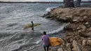 Di pantai Kota Gaza, beberapa warga Palestina menemukan kembali kenikmatan berselancar. Tampak dalam foto, warga Palestina, Khalil Abu Jayyab (depan) dan Tahseen Abu Assi membawa papan selancar mereka saat memasuki sepanjang garis pantai di Kota Gaza, Minggu, 28 Desember 2025. (AP Photo/Jehad Alshrafi)