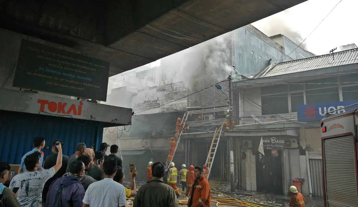 Sejumlah warga menyaksikan petugas pemadam kebakaran memadamkan api yang membakar gudang petasan di jalan Asemka, Jakarta, Jumat (21/6/2019). Sebanyak 27 unit mobil dinas pemadam kebakaran dikerahkan untuk memadamkan gudang penyimpanan petasan itu. (Liputan6.com/Herman Zakharia)