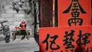 Seorang anak berpose untuk difoto di samping kuplet musim semi, semacam dekorasi Tahun Baru Imlek, jelang dimulainya Tahun Baru Imlek di sebuah kios di Foshan, Provinsi Guangdong, China, 18 Januari. Format dan ritme kuplet harus identik atau saling melengkapi. (Giok Gao/AFP)