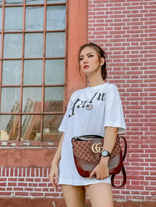 Nita Gunawan mengenakan oversized shirt berwarna putih untuk kesan santai dan kasual. Ia pun menjinjing crossbody bag dari Gucci untuk memberikan kesan mewah. (instagram/nitagunawan09)