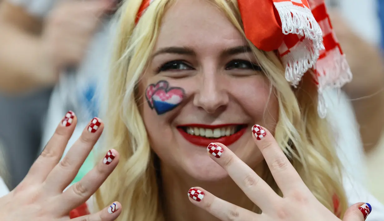 Seorang Fans wanita menunjukkan kukunya dicat dengan warna bendera Kroasia saat dia bersorak jelang dimulainya pertandingan semifinal Piala Dunia Qatar 2022 antara Argentina dan Kroasia di Stadion Lusail di Lusail, utara Doha, Rabu (14/12/2022). (AFP/Jack Guez)