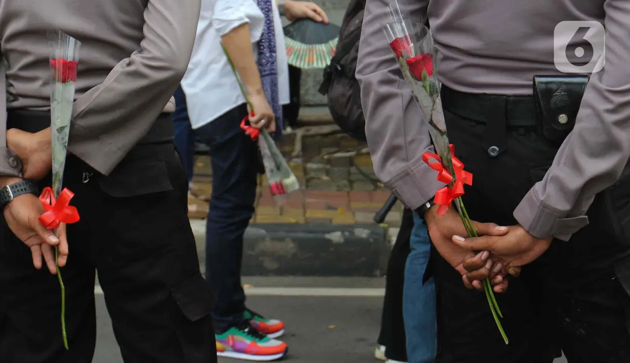 Petugas kepolisian memegang bunga mawar saat menjaga peserta aksi seruan damai di depan Kedutaan Besar Federasi Rusia, Jakarta, Rabu (30/3/2022). Aksi mengangkat tema "Setangkai Kembang dan Satu Nyanyian" dengan membawakan lagu Rayuan Pulau Kelapa versi bahasa Rusia. (Liputan6.com/Herman Zakharia)