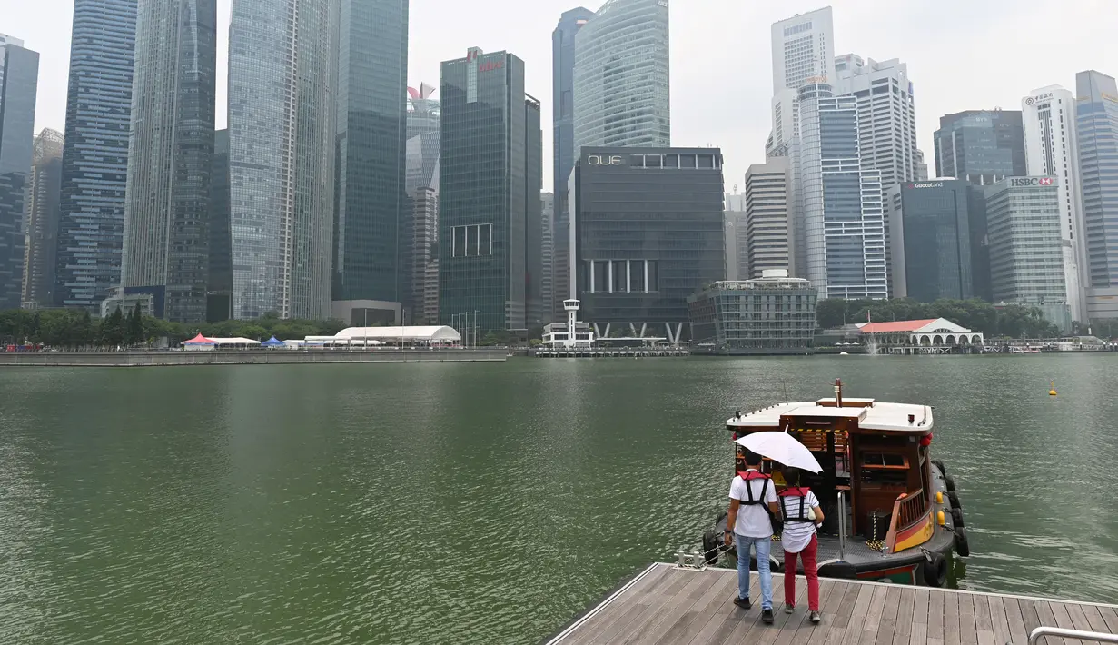 Dua orang bersiap menaiki perahu saat deretan gedung diselimuti kabut asap di Marina Bay, Singapura (13/9/2019). Titik api di hutan hujan Indonesia telah melonjak tajam, data satelit menunjukkan pada 12 September, menyebarkan kabut asap di Asia Tenggara. (AFP Photo/Roslan Rahman)