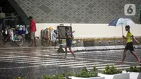Anak-anak yang bekerja sebagai ojek payung menyeberang jalan saat hujan deras di kawasan Thamrin, Jakarta, Rabu (23/11/2022). Sejak Oktober, DKI Jakarta mulai memasuki musim penghujan yang sudah masuk ke dalam tahap ekstrem. (Liputan6.com/Faizal Fanani)