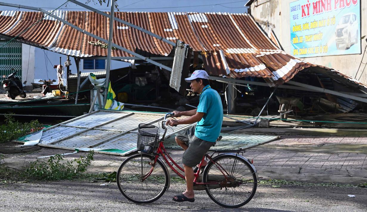 Vietnam maupun Filipina menjadi negara yang paling rentan terhadap badai tropis karena berada di jalur sabuk topan pasifik. Tampak dalam foto, seorang pria mengayuh sepeda melewati struktur atap yang sebagian runtuh di kawasan pesisir Quy Nhon, Provinsi Gia Lai, Vietnam Tengah, pada Jumat 7 November 2025. (NHAC NGUYEN/AFP)