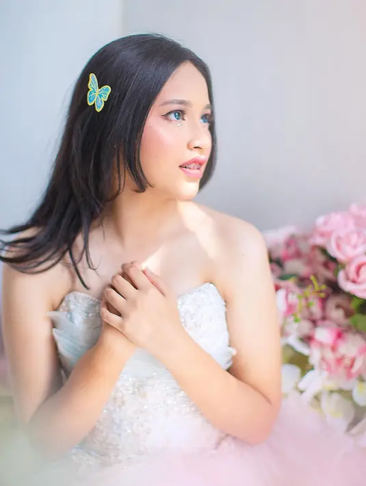 Rambut yang digerai dengan tambahan aksesori simpel bentuk kupu-kupu membuat Shakiena terlihat imut. Ketika jalani pemotretan tersebut, Shakiene kenakan beberapa model gaun berbeda. Setelah sebelumnya pakai gaun warna biru dengan renda, kemudian Shakiena kenakan gaun warna putih yang elegan. Tidak terlihat berlebihan, Shakiena cocok kenakan gaun tersebut. (Liputan6.com/IG/@okieagustina_)
