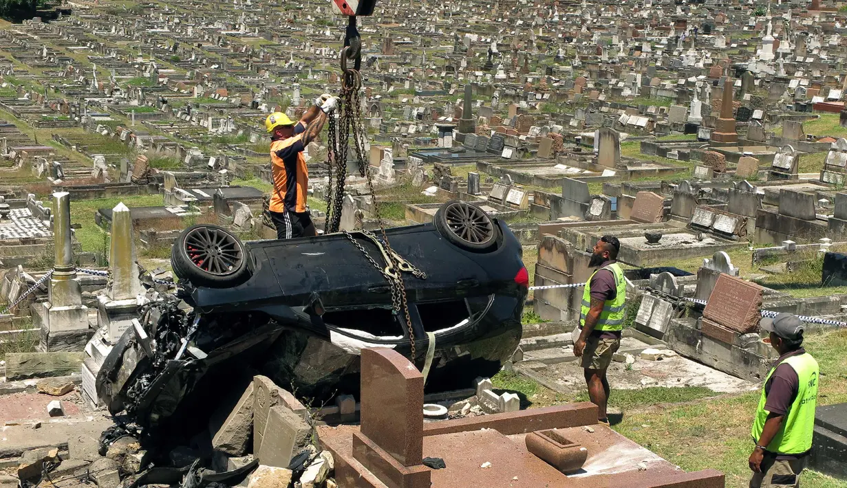 Petugas mengangkat mobil SUV Mercedes usai menabrak nisan di sebuah pemakaman di pinggiran selatan South Coogee, Australia (6/2). Akibat kecelakaan tersebut lebih dari 10 batu nisan hancur. (AFP Photo/William West)