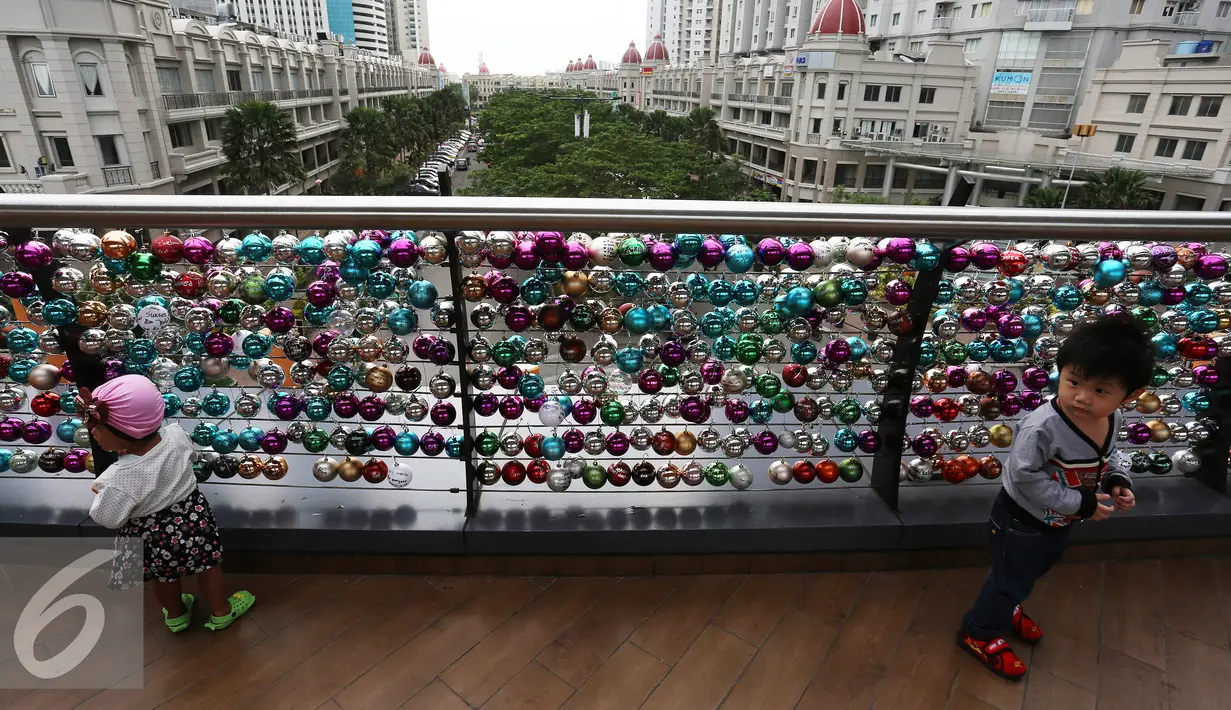 Anak-anak bermain di depan ribuan Bola bertuliskan harapan yang tergantung di pagar jembatan Eco Skywalk di Mall Central Park, Jakarta, Senin (19/12). Pengunjung dapat membeli Bola Pengharapan dengan harga Rp. 10.000. (Liputan6.com/Johan Tallo)