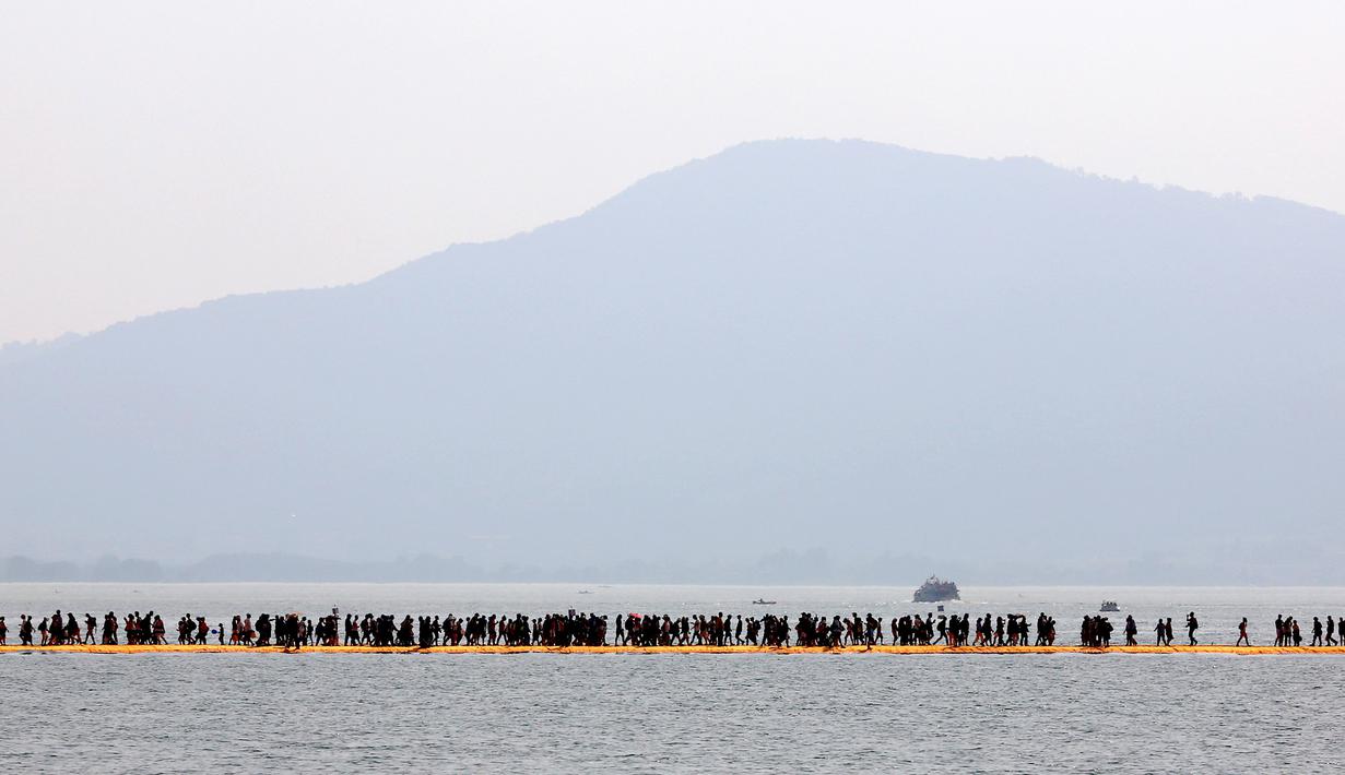 Wisatawan berjalan di atas instalasi "The Floating Piers" di Danau Iseo, Italia, (24/6). Seni instalasi yang mengambang di atas Danau Iseo menghubungkan Desa Sulzano ke pulau kecil Monte Isola yang berada di tengah danau. (REUTERS/Stefano Rellandini)