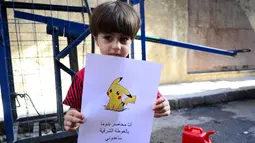 Seorang bocah memegang kertas bergambarkan karakter Pokemon serta tulisan "Aku terjebak di Douma di Timur Ghouta. Bantu aku", Suriah (22/7). (REUTERS)