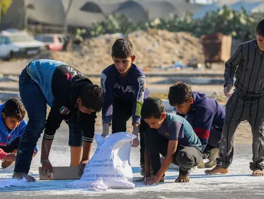 Anak laki-laki Palestina mengais tepung dari jalan setelah sebuah tas jatuh dari truk bantuan yang melaju di jalan Salaheddin di Deir el-Balah di Jalur Gaza tengah pada 5 November 2024. (Eyad BABA/AFP)