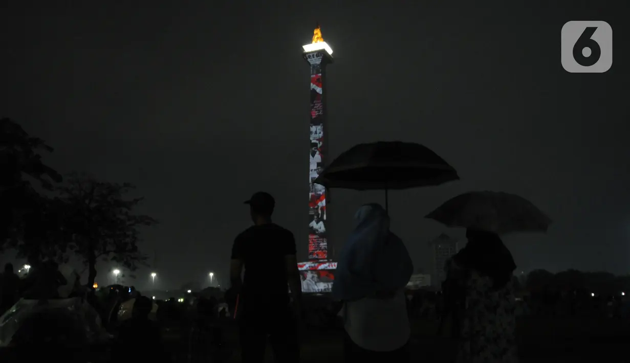 Pengunjung menyaksikan penampilan video mapping saat malam pergantian tahun di kawasan Monumen Nasional, Jakarta, Selasa (31/12/2019). Meski Jakarta diguyur hujan sejak Selasa (31/12) sore, warga tetap mendatangi kawasan Monas untuk merayakan malam pergantian tahun. (Liputan6.com/Helmi Fithriansyah)