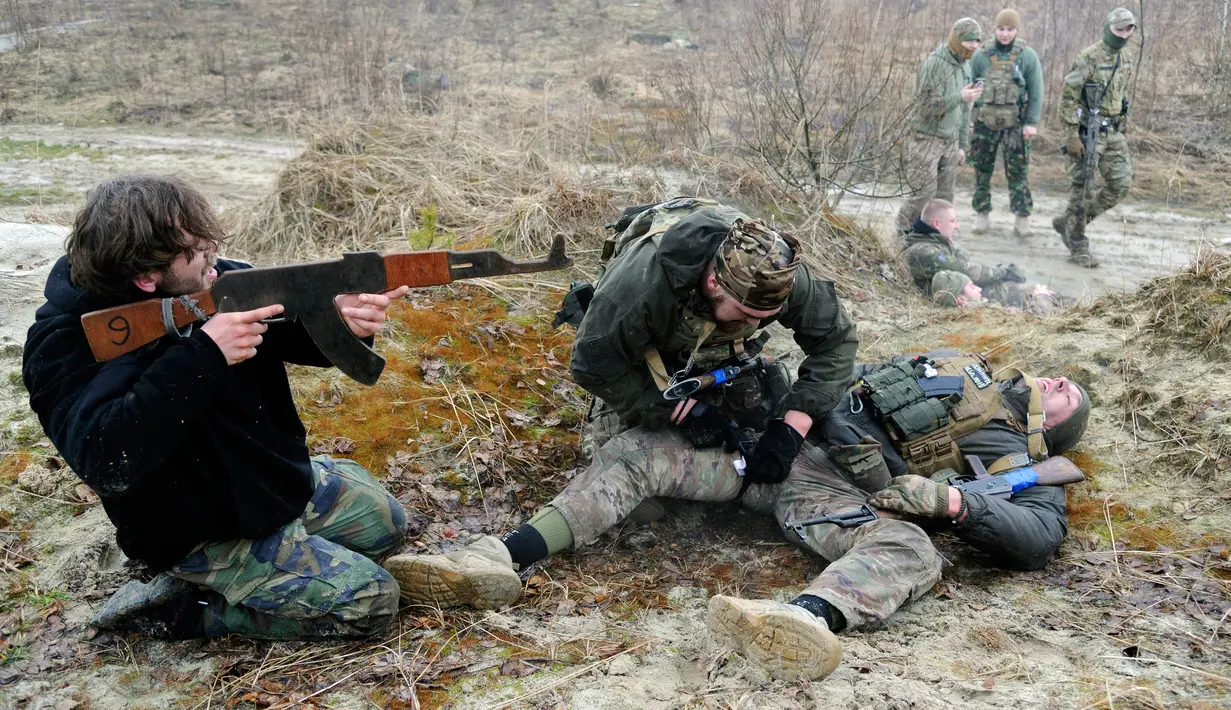 Warga sipil berlatih menembak sementara rekannya melakukan pengobatan prajurit yang terluka saat mengikuti sesi pelatihan militer oleh Right Sector dekat Lviv, Ukraina, 24 Februari 2023. (AP Photo/Mykola Tys)