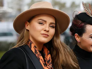 Dua pengunjung wanita, tampil cantik dengan topi di kepalanya jelang pembukaan ajang Pacuan Kuda dalam Festival Cheltenham di Inggris (16/3). Pacuan kuda merupakan olahraga yang disukai oleh kerajaan Inggris. (REUTERS/Paul Childs)