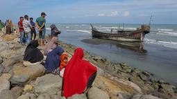 Penduduk desa melihat perahu kayu yang digunakan oleh orang-orang Rohingya di Pidie, provinsi Aceh pada 27 Desember 2022. Pengungsi Rohingya menerima perawatan medis darurat setelah sebuah kapal yang membawa hampir 200 orang mendarat di Indonesia pada 26 Desember, kata pihak berwenang, dalam pendaratan keempat di negara dalam beberapa bulan terakhir. (AFP/Amanda Jufrian)