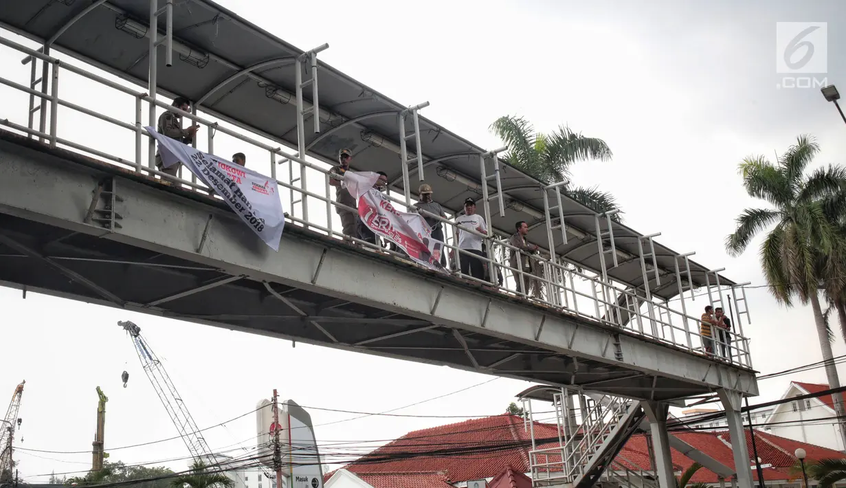 Petugas Satpol PP mencopot alat peraga kampanye (APK) berupa spanduk caleg di JPO kawasan Gambir, Jakarta, Sabtu  (22/12). PenertiBan spanduk APK dilakukan karena melanggar aturan pemasangan dari komisi pemilihan umum. (Liputan6.com/Faizal Fanani)
