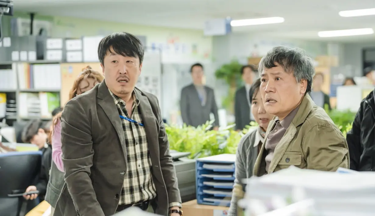 Dalam potongan gambar pertama, pejabat Balai Kota Onju sedang berkonfrontasi dengan beberapa pelapor. Lee Hong Jo tampaknya terjebak di antara ketua tim divisi Gong Seo Gu (Hyun Bong Sik) dan para pengadu yang marah. (JTBC via Soompi)