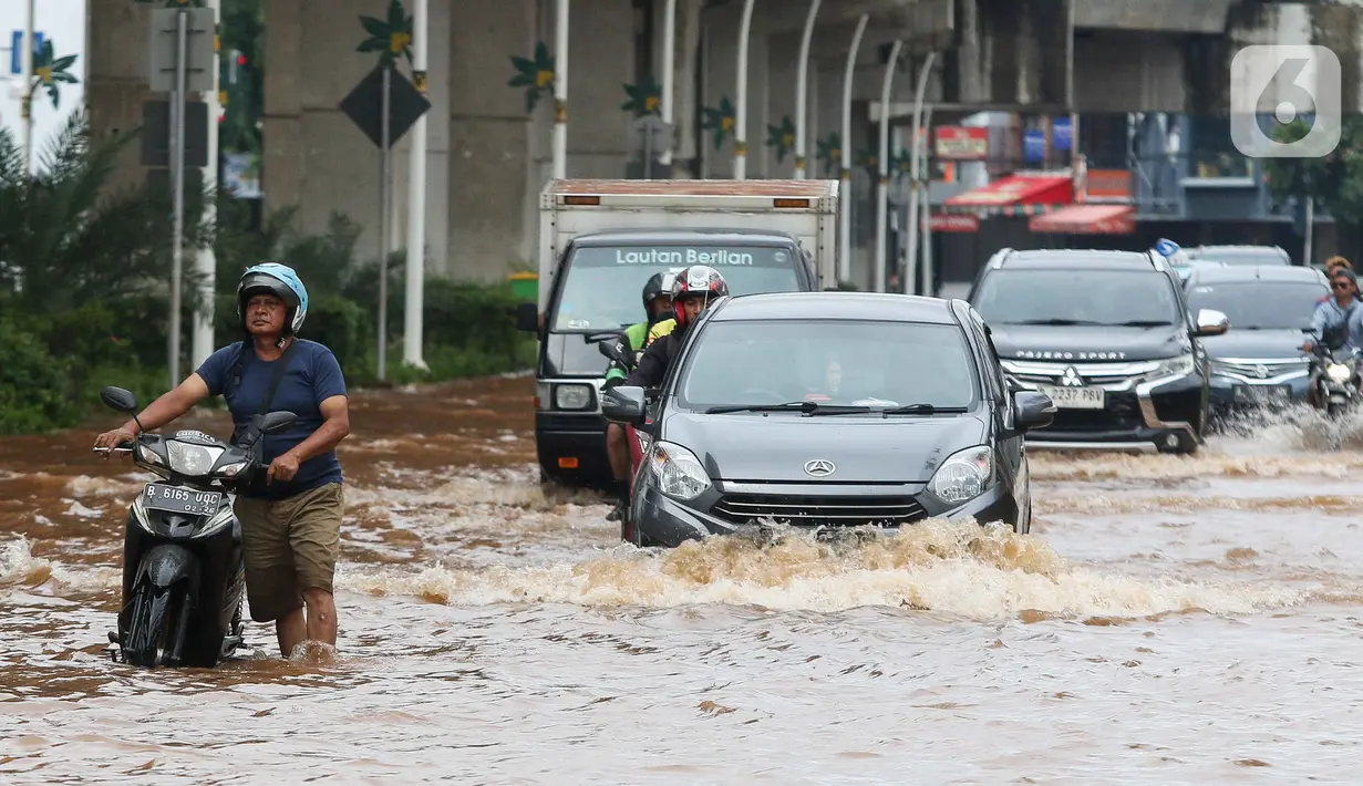 Pengendara terpaksa mendorong motornya saat melintasi genangan air di Jalan Boulevard Raya, Kelapa Gading, Jakarta, Rabu (29/1/2025). (Liputan6.com/Herman Zakharia)