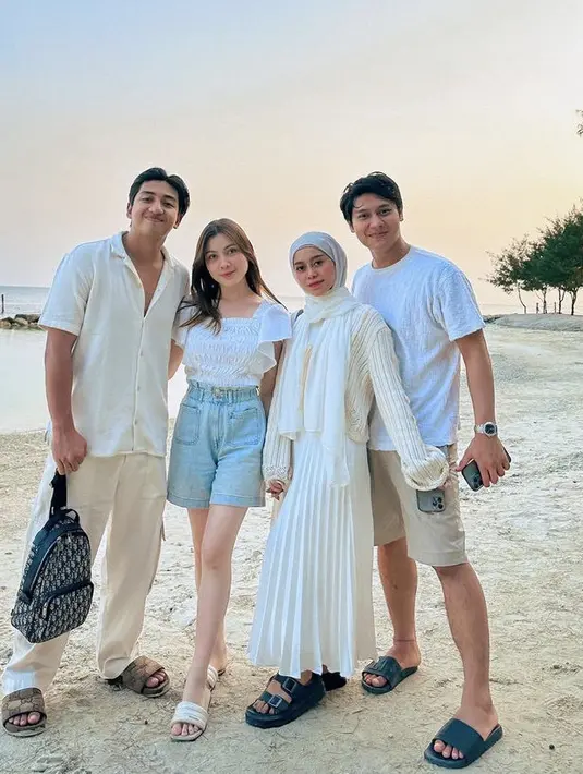 Berada di pantai bersama suami dan temannya, Lesti tampil serba putih mengenakan atasan lengan panjang, rok panjang plisket, dan pashmina nya. (@lestykejora)