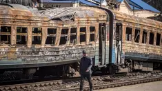 Seorang pria berjalan di depan kereta api yang hancur di timur laut kota Trostianets (29/3/2022). Ukraina mengatakan pasukannya telah merebut kembali kota Trostianets, dekat perbatasan Rusia, salah satu kota pertama yang jatuh di bawah Kontrol Moskow dalam invasi selama sebulan. (AFP/Fadel Senna)