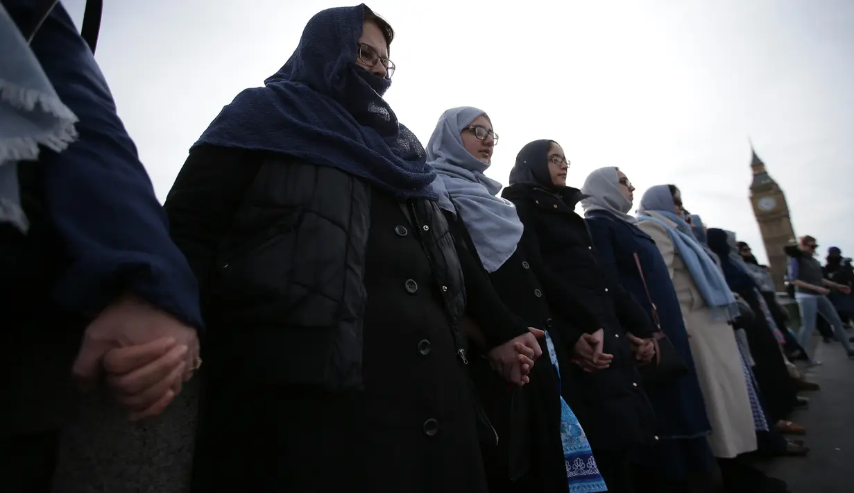 Puluhan perempuan dari beragam etnis bergandengan tangan di Jembatan Westminster, dekat Gedung Parlemen Inggris, London, Minggu (26/3). Mereka mengheningkan cipta selama lima menit untuk mengenang para korban serangan teror London (Daniel LEAL-OLIVAS/AFP)