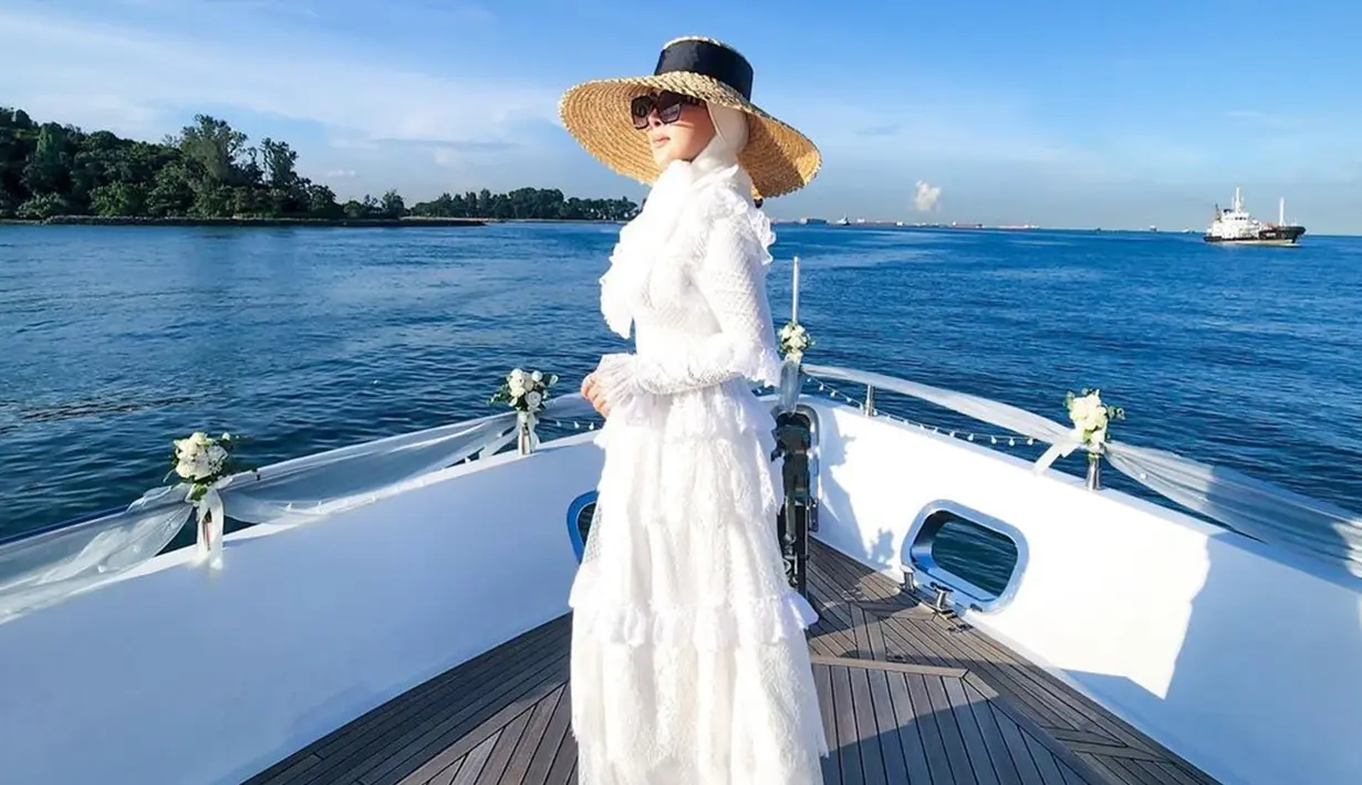 Gaya Syahrini saat berlayar pun begitu elegan. Wanita berusia 40 tahun itu mengenakan gaun putih panjang penuh renda. Sebagai pelengkap penampilannya, penyanyi yang pernah populer dengan 'jambul khatulistiwa' itu memakai topi bundar ala pantai dan kacamata hitam. (Liputan6.com/IG/@princessyahrini)