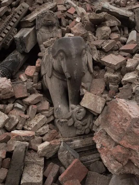 Patung berdiri di antara puing-puing kuil bersejarah yang hancur akibat gempa berkekuatan 7,8  di sekitar Kathmandu, Nepal  (30/4/2015). Lebih dari 5.000 orang tewas akibat gempa yang meluluhlantakkan Nepal pada 25 April 2015 lalu. (Nicolas Asfouri/AFP)