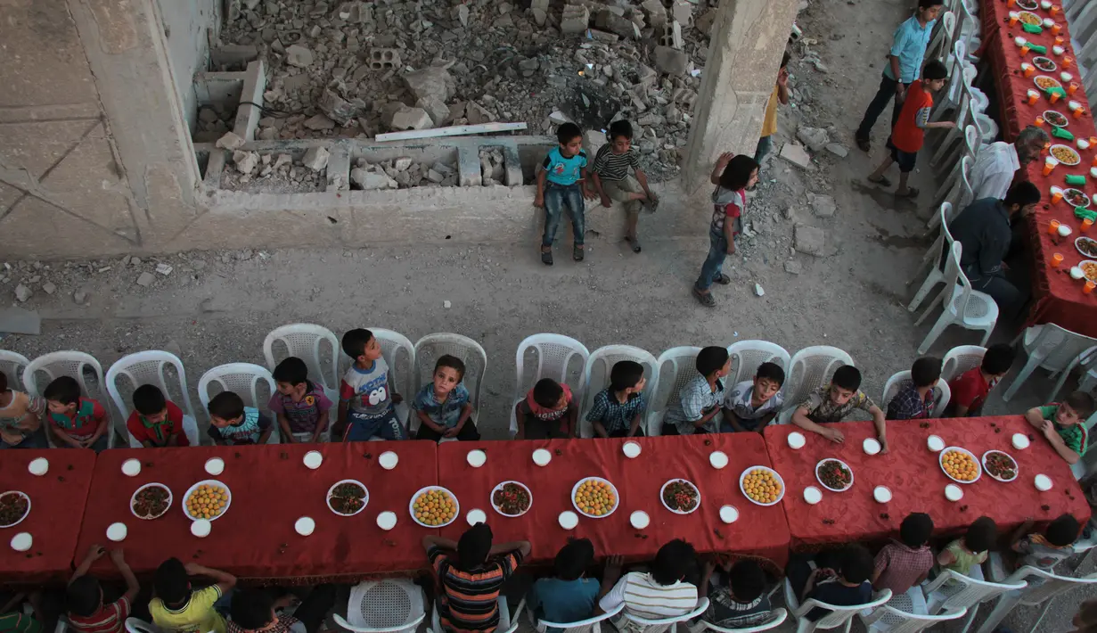 Sejumlah anak bersiap untuk berbuka puasa bersama di tengah reruntuhan bangunan di Kota Douma, yang dikuasai pemberontak di pinggiran ibukota Damaskus, Suriah, (18/6). (AFP Photo/Hamza Al-Ajweh)