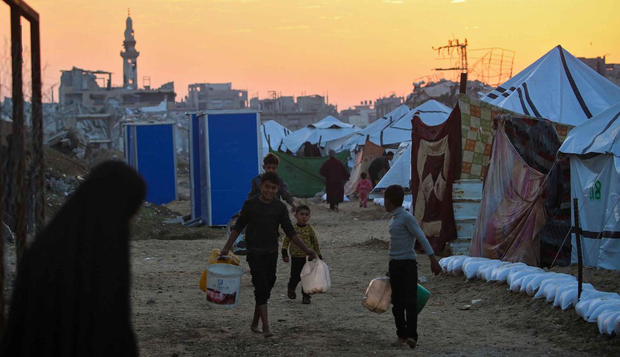 Kondisi ini memaksa warga Gaza bergantung pada distribusi bantuan air bersih dengan jumlah yang terbatas. Tampak dalam foto, anak-anak membawa air di kamp Nuseirat untuk pengungsi Palestina di Jalur Gaza tengah pada Kamis 4 Desember 2025. (Eyad Baba/AFP)