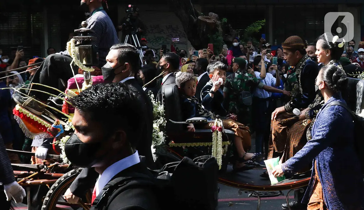 Presiden Joko Widodo didampingi Ibu Negara Iriana Joko Widodo menaiki kereta dalam mengikuti prosesi kirab Ngunduh Mantu di kawasan Selamet Riyadi, Solo, Jawa Tengah, Minggu (11/12/2022). Kirab ngunduh mantu pernikahan putra bungsu Presiden Joko Widodo, Kaesang Pangarep dan istrinya Erina Gudono yang dimulai dari Loji Gandrung menuju Pura Mangkunegaran tersebut disaksikan ribuan masyarakat Solo dan sekitarnya. (Liputan6.com/Herman Zakharia)