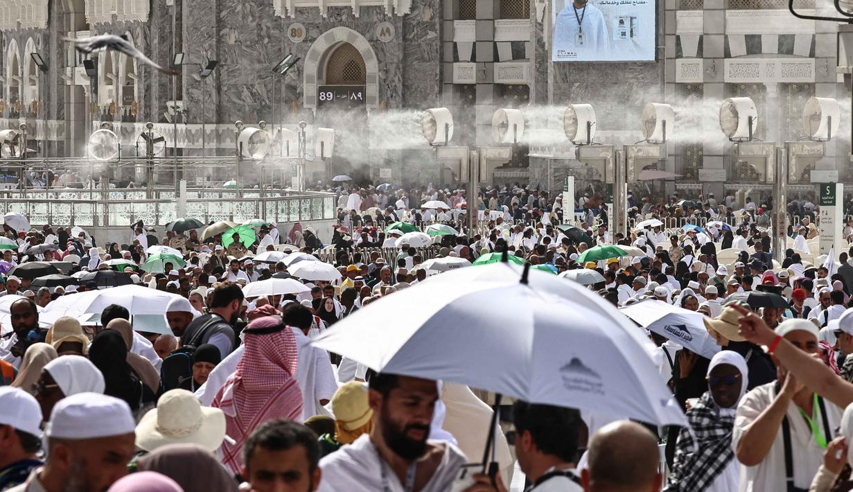 Para jamaah Muslim berjalan di sepanjang kompleks Masjidil Haram di bawah kipas kabut air yang dipasang di kota suci Mekah pada Minggu 24 Mei 2026, menjelang ibadah haji tahunan. (Zain JAAFAR/AFP)