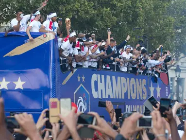 Timnas Prancis mengikuti pawai dengan bus atap terbuka merayakan juara Piala Dunia 2018 di sepanjang Champs Elysees, Paris, Senin (16/7). Prancis menggelar pesta besar penyambutan sekaligus parade kemenangan bagi skuad ”Les Bleus”. (AP/Claude Paris)