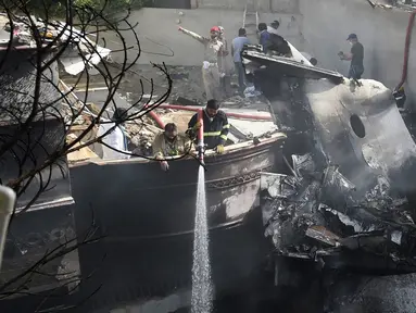 Petugas pemadam kebakaran menyemprotkan air pada puing pesawat Pakistan International Airlines yang jatuh di Karachi, Pakistan, Jumat (22/5/2020). Menurut perwakilan dari Kementerian Kesehatan Sindh, 97 orang dilaporkan meninggal dan dua orang selamat dalam kecelakaan tersebut. (Rizwan TABASSUM/AFP)